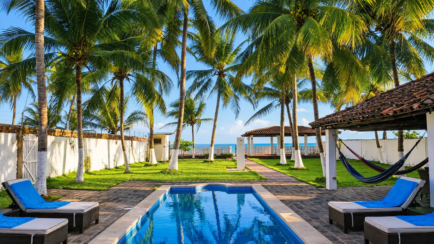 Piscina con palmeras, jardín y el mar al fondo
